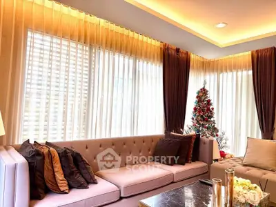 Elegant living room with plush sofa and Christmas tree, featuring large windows and soft lighting.