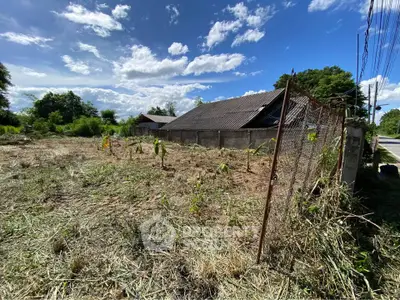 Spacious land plot with rustic building and lush greenery under a clear blue sky.