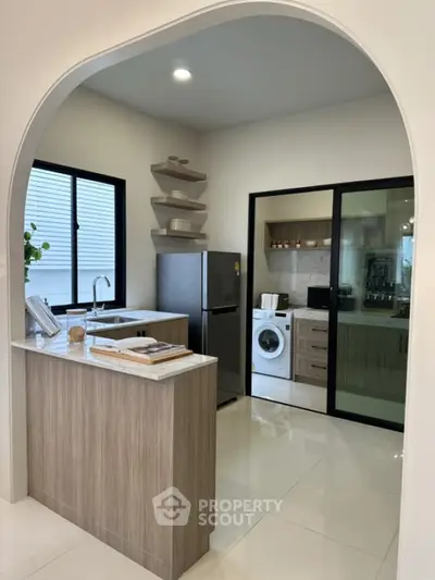 Modern kitchen with sleek design, featuring a washing machine and refrigerator in a bright open layout.