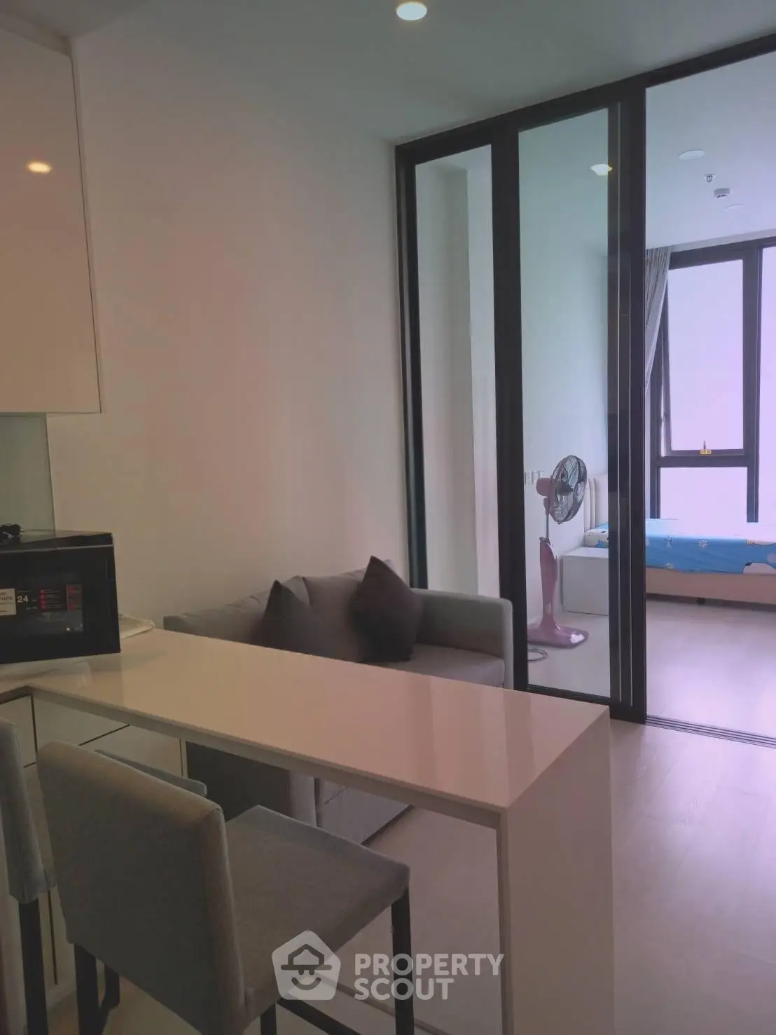 Modern apartment interior with sleek kitchen and cozy living area, featuring a glass partition leading to a bedroom.