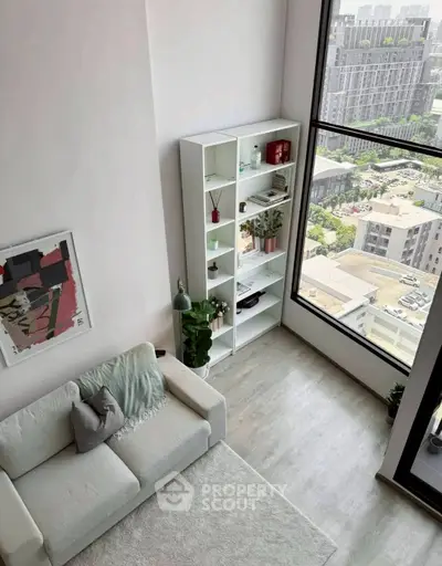 Modern living room with large window and city view, featuring a cozy white sofa and stylish decor.