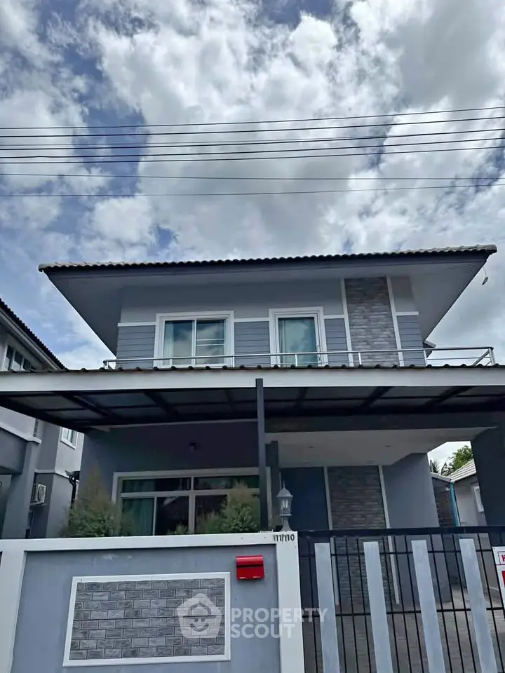 Modern two-story house with stylish facade and gated entrance under a cloudy sky.