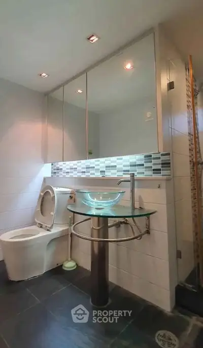 Modern bathroom with glass sink and tiled shower in sleek apartment.