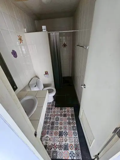 Compact bathroom with tiled walls and decorative floor tiles, featuring a shower and toilet.