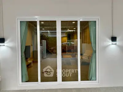 Modern living room with large sliding glass doors and elegant curtains, offering a glimpse of a cozy interior.