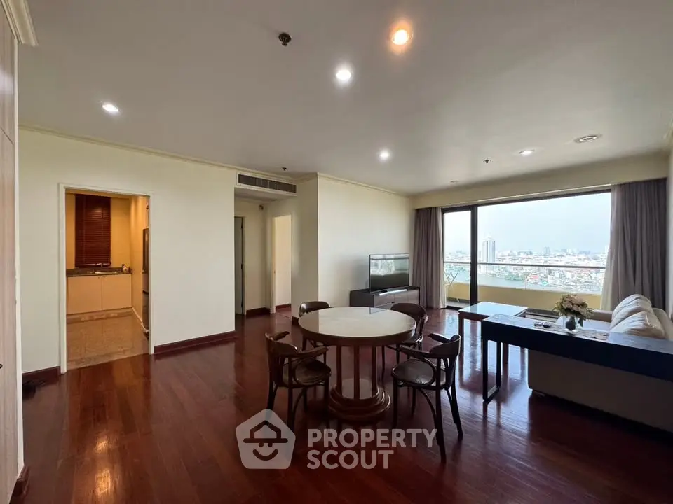 Spacious living room with wooden flooring and city view, featuring a dining area and cozy seating.