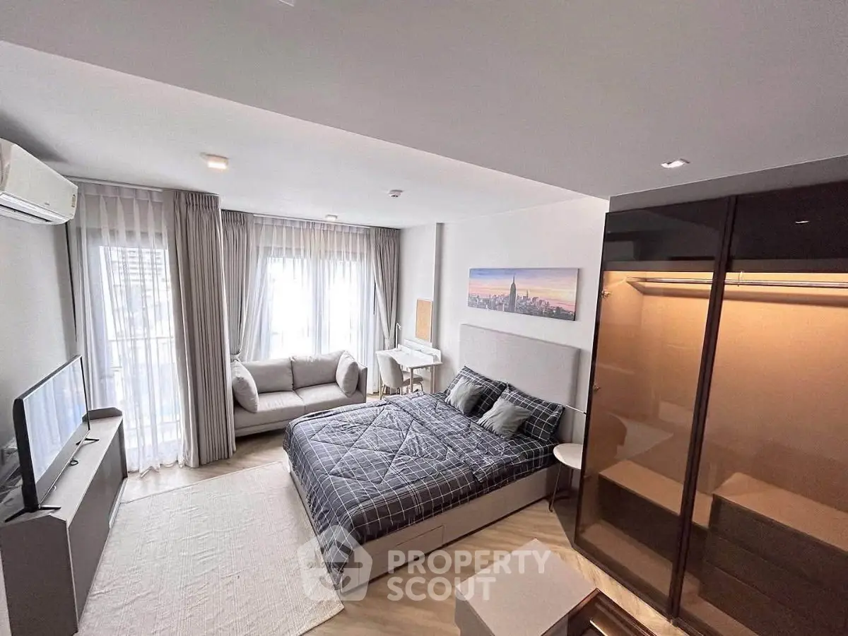 Modern bedroom with stylish decor, large windows, and cozy seating area in a contemporary apartment.