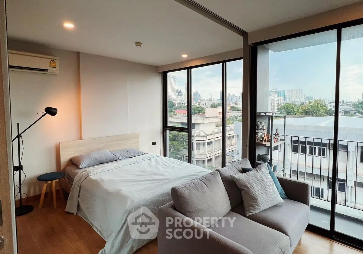 Modern bedroom with city view, featuring a cozy bed and stylish sofa in a high-rise apartment.