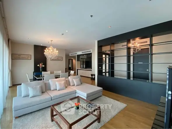 Spacious modern living room with elegant decor and open layout, featuring a large sofa and chandelier lighting.