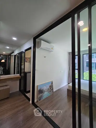 Modern apartment interior with glass partitions and wooden flooring, featuring a cozy bedroom and air conditioning.