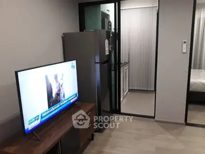 Modern apartment interior with sleek kitchen and cozy living area featuring a flat-screen TV and refrigerator.