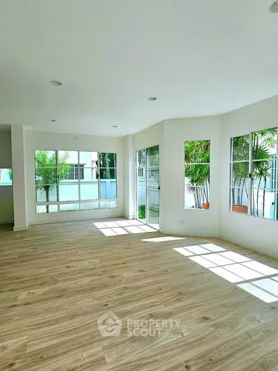 Spacious sunlit living room with large windows and wooden flooring