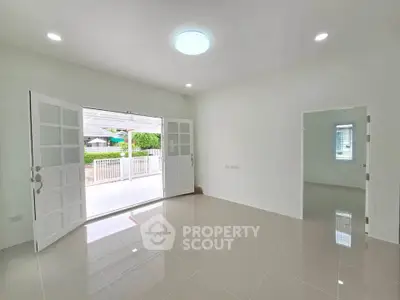 Spacious modern living room with open doors to a bright patio, featuring sleek tile flooring and ample natural light.