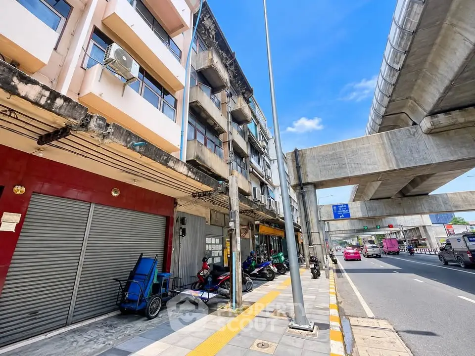 Urban street view with mixed-use buildings and elevated road in vibrant city setting.