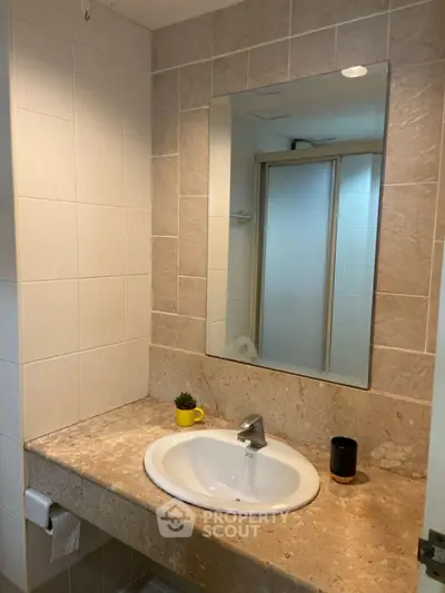 Modern bathroom with elegant sink and large mirror, featuring stylish beige tiles.