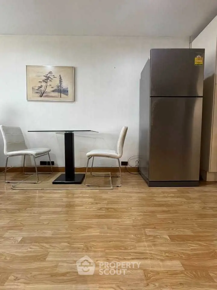 Modern dining area with sleek table, chairs, and stainless steel fridge on wooden flooring.