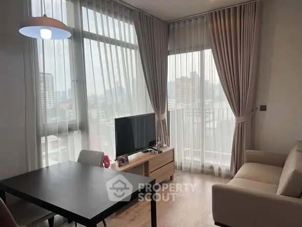 Modern living room with large windows and city view, featuring a cozy sofa and sleek TV setup.