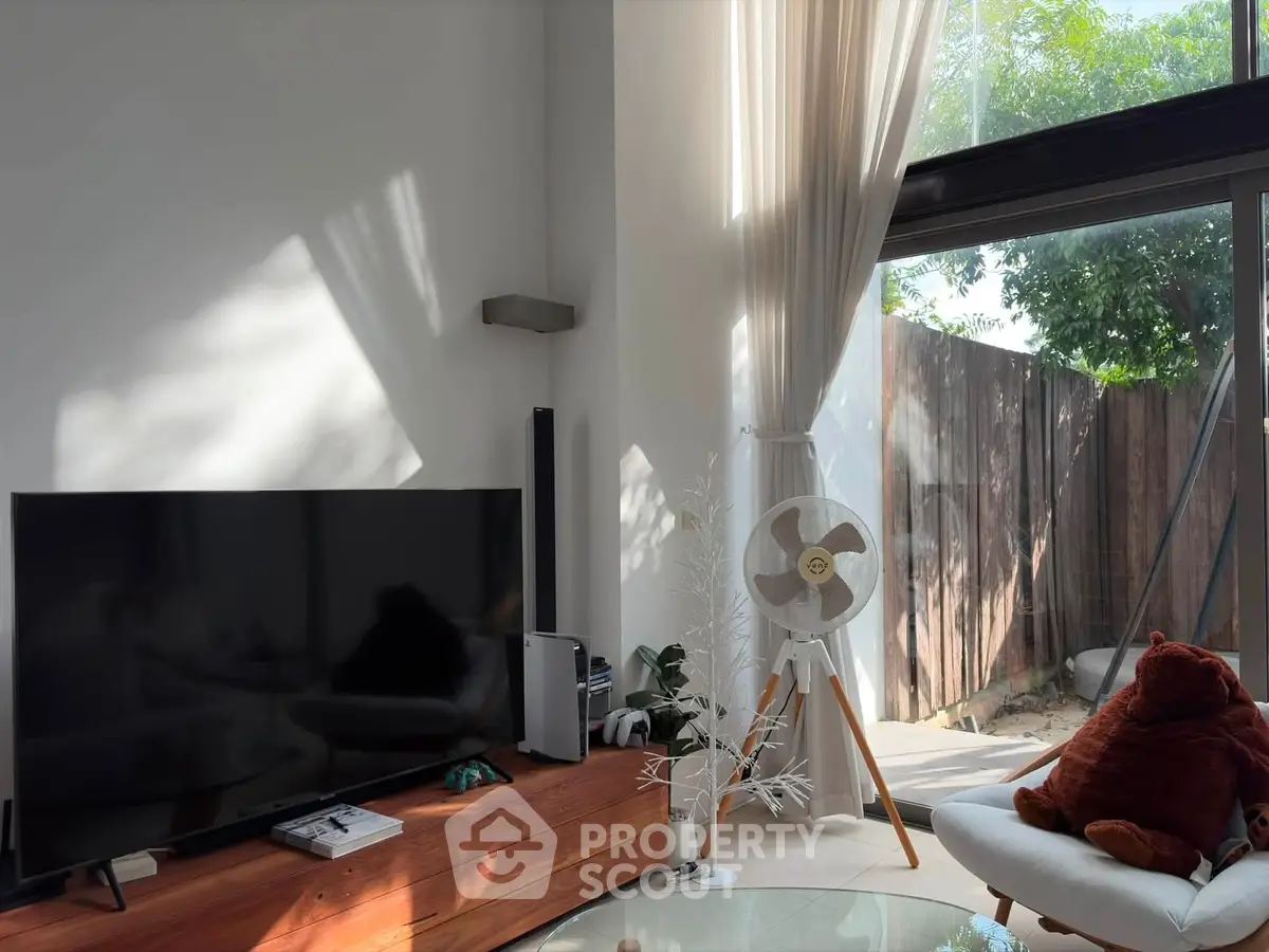 Modern living room with large TV, stylish decor, and natural light from floor-to-ceiling windows.
