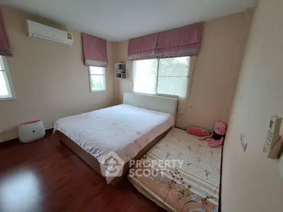 Cozy bedroom with large bed and additional mattress, featuring wooden flooring and air conditioning.