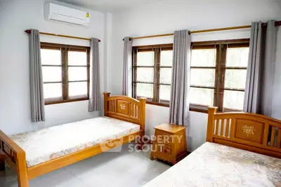 Bright bedroom with twin wooden beds and large windows, perfect for natural light lovers.