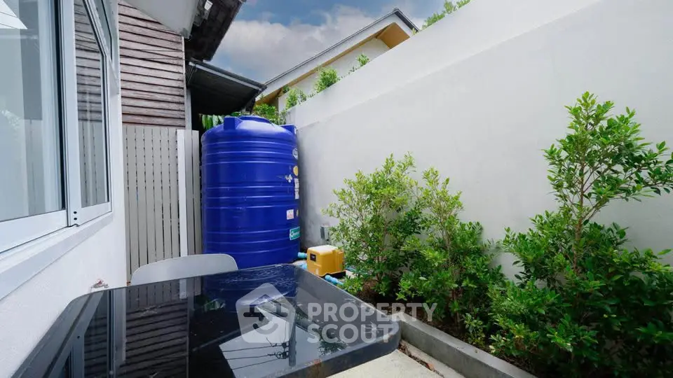 Charming outdoor patio with lush greenery and modern water tank, perfect for relaxation and sustainability.