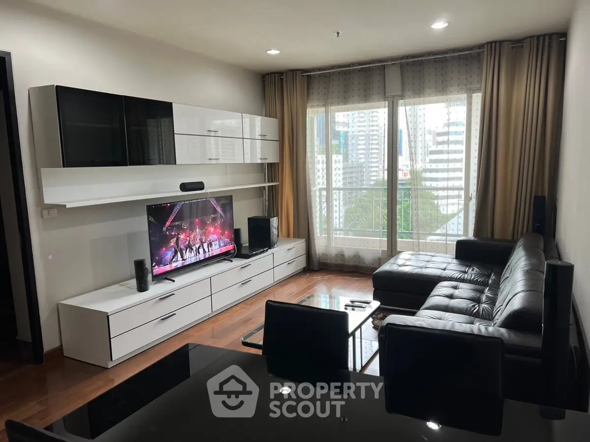 Modern living room with sleek black leather sofa and large TV, featuring city view from window.