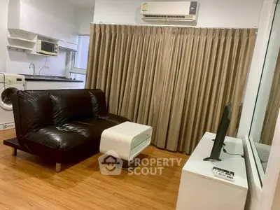 Modern living room with black leather sofa, TV, and compact kitchen area.