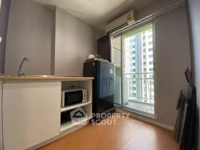 Compact kitchen with microwave and mini fridge, adjacent to a balcony with city view.
