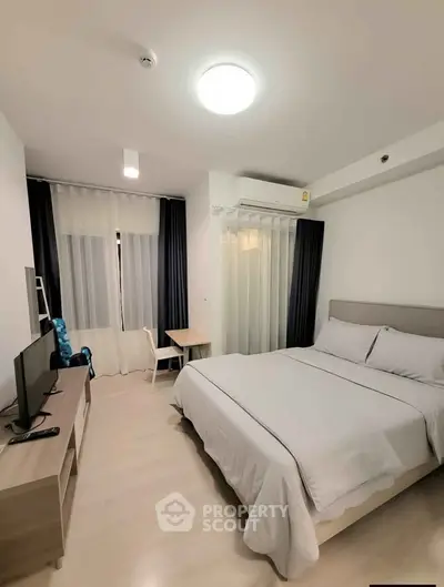 Modern bedroom with cozy bed, TV, and study desk in a bright apartment.