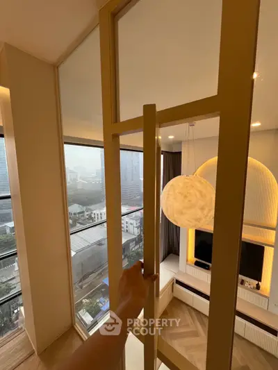Modern living room with large windows offering city view, stylish lighting, and elegant decor.