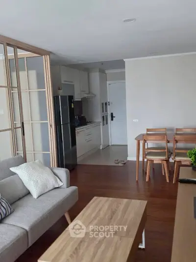 Modern open-layout living room with kitchen, featuring sleek furniture and wooden accents.