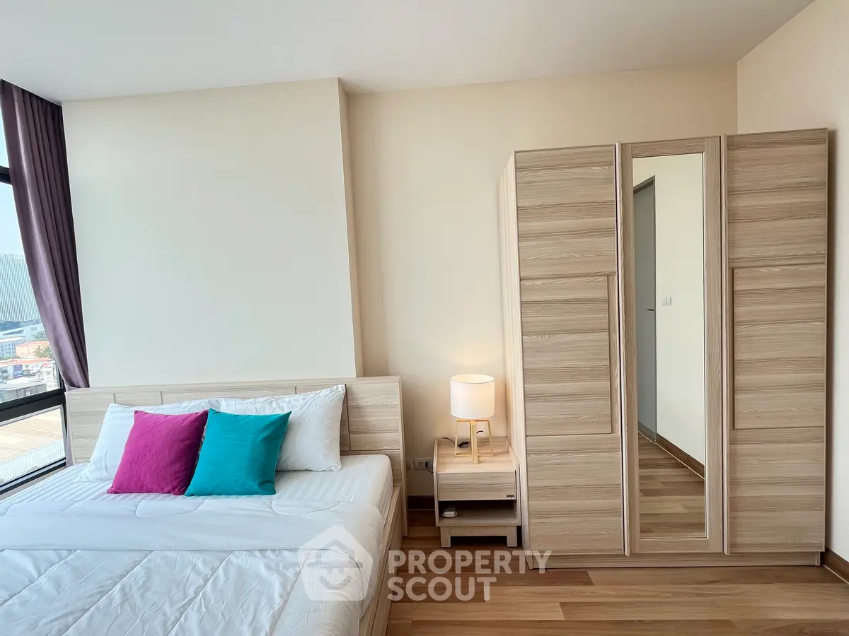 Modern bedroom with wooden flooring, stylish wardrobe, and cozy bed with colorful pillows.