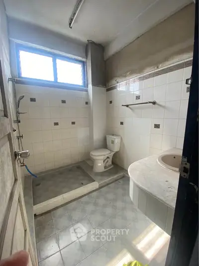 Spacious bathroom with tiled walls and floor, featuring a toilet and shower area.