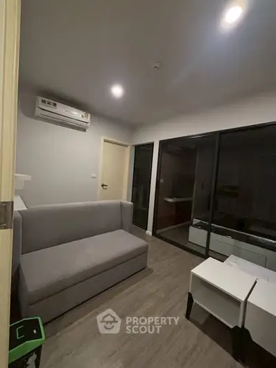 Modern living room with sleek gray sofa and glass partition, featuring minimalist design and air conditioning.