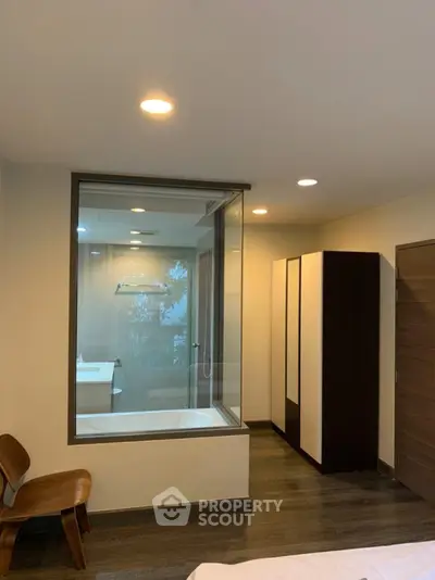 Modern bedroom with glass partition revealing a stylish bathroom and sleek furniture.