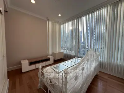 Spacious bedroom with large windows offering stunning city views and elegant decor.
