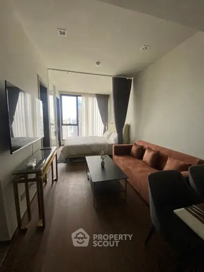 Modern studio apartment with cozy living area and large windows offering city views.