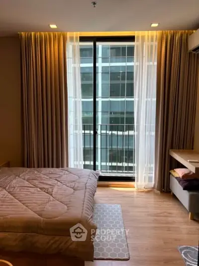 Modern bedroom with large window and city view, featuring cozy bedding and elegant curtains.