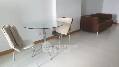 Modern living room with glass table and cozy brown sofa in a bright, tiled space.