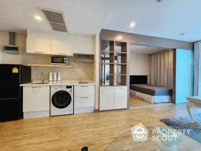 Modern open-plan studio apartment with kitchen and bedroom area, featuring wooden flooring and stylish decor.