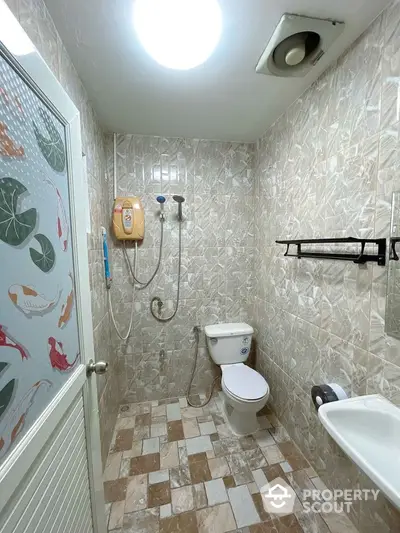 Compact bathroom with shower and toilet in tiled interior