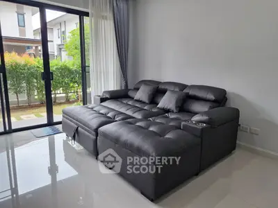 Spacious living room with modern black leather sectional sofa and large windows overlooking garden.