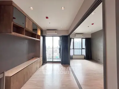 Spacious modern living room with large windows and city view, featuring sleek wooden cabinetry.