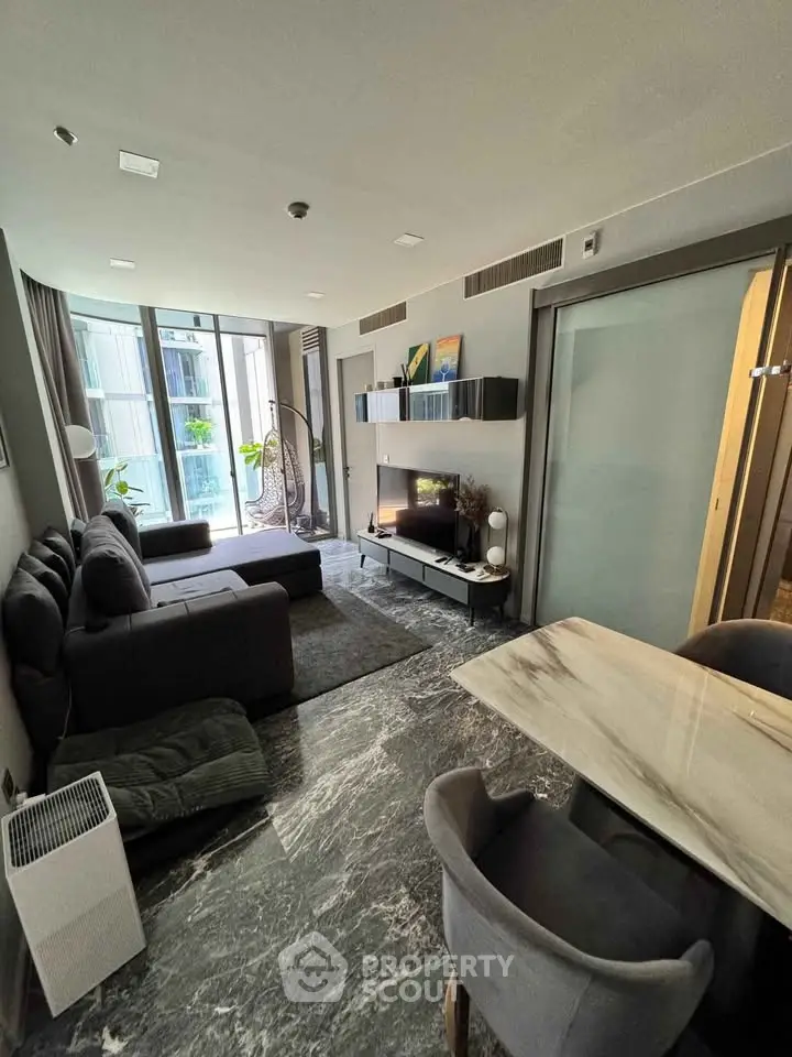 Modern living room with sleek furniture and large windows offering natural light and a city view.
