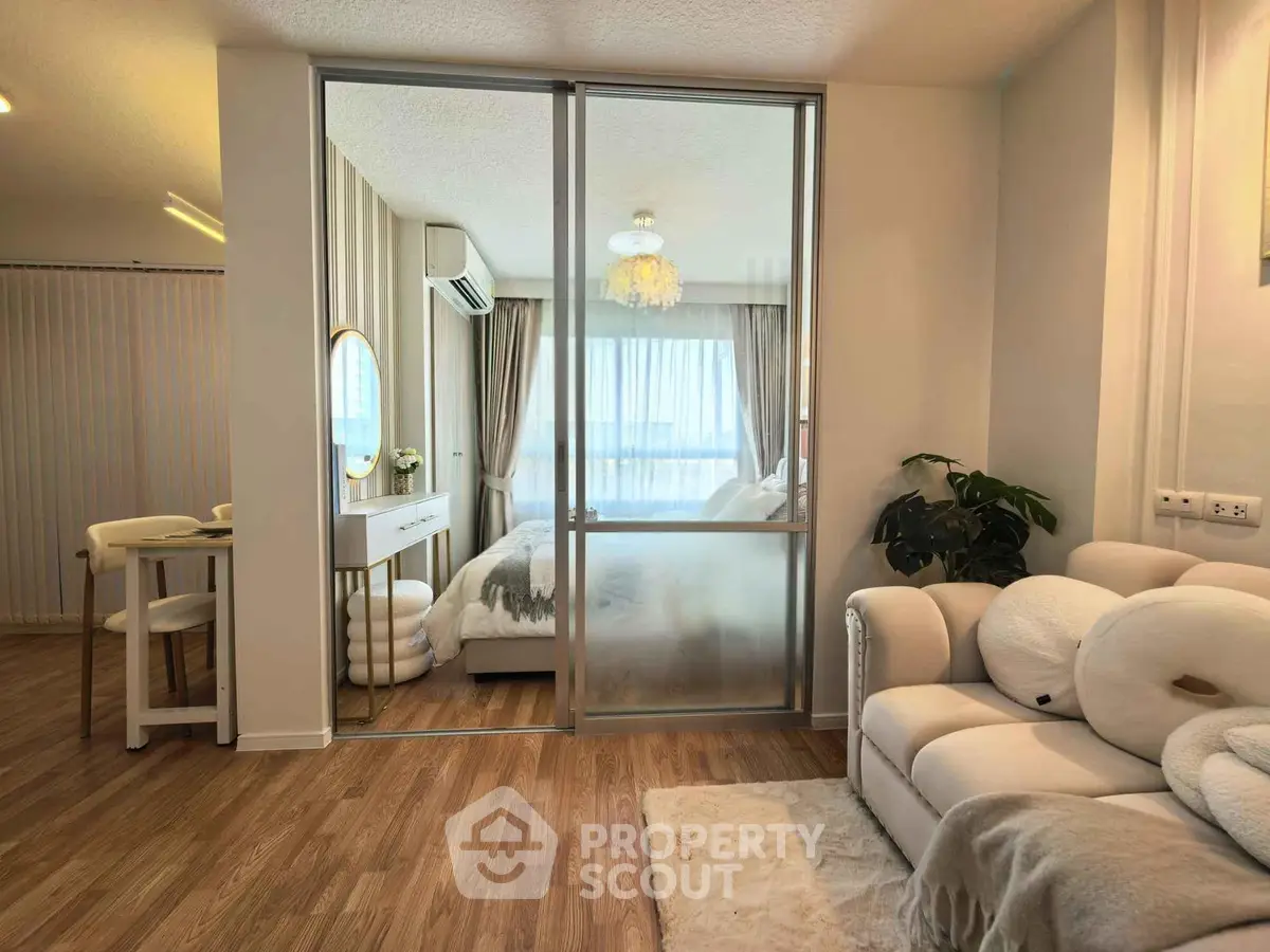 Modern living room with cozy seating and view into elegant bedroom through glass partition.