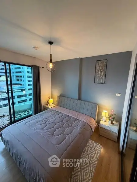 Modern bedroom with cozy decor and city view from large window.
