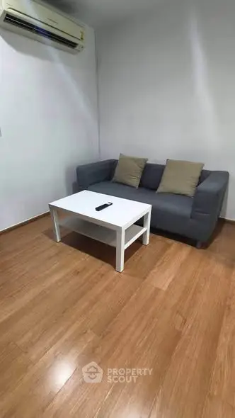Cozy living room with modern sofa and coffee table, featuring wooden flooring and air conditioning.
