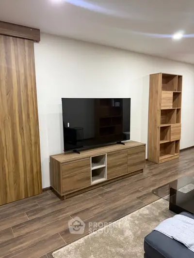 Modern living room with sleek wooden furniture and large flat-screen TV, perfect for relaxation and entertainment.
