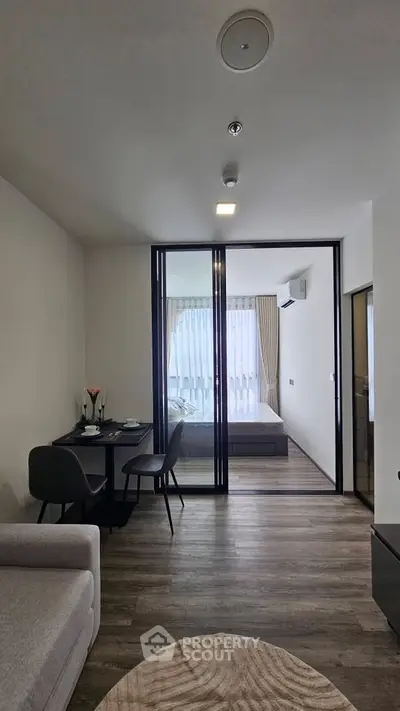 Modern apartment interior with open living and dining area leading to a cozy bedroom.