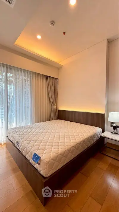 Modern bedroom with elegant lighting and large window, featuring a stylish bed and wooden flooring.